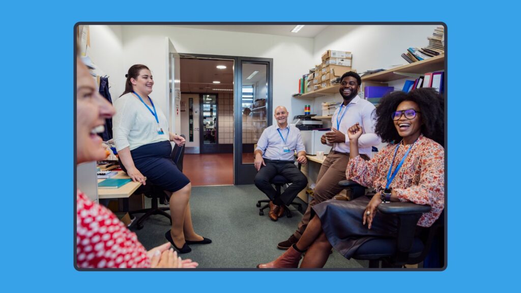 A group of diverse teachers laughing and talking in a school office